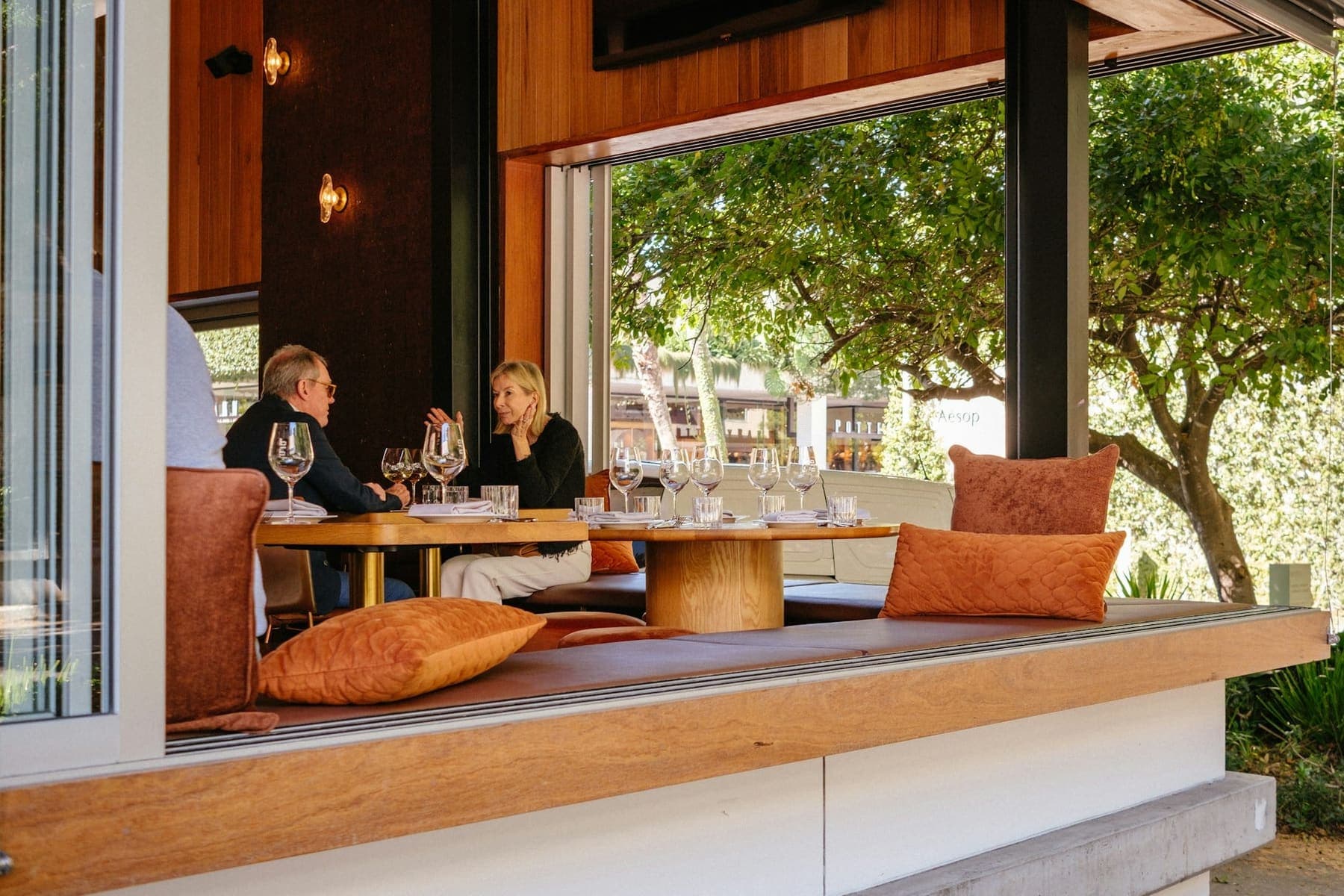 Guests talking over a wine flight at a sunlit restaurant table with warm wood and upholstered seating