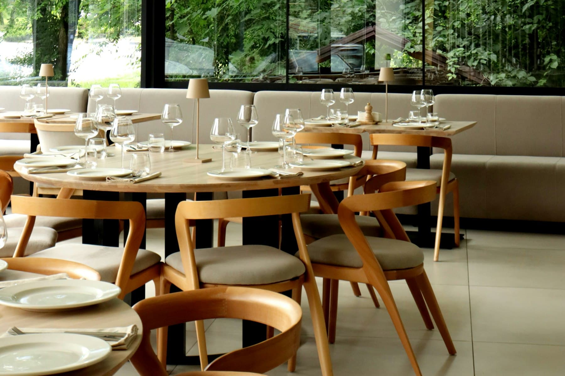 Sunlit dining room with set tables, wine glasses, upholstered seating, and space between chairs