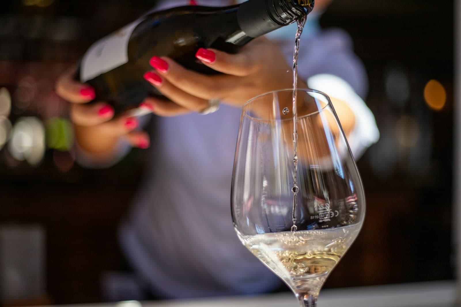 A server pours white wine into a stemmed glass at a dining table