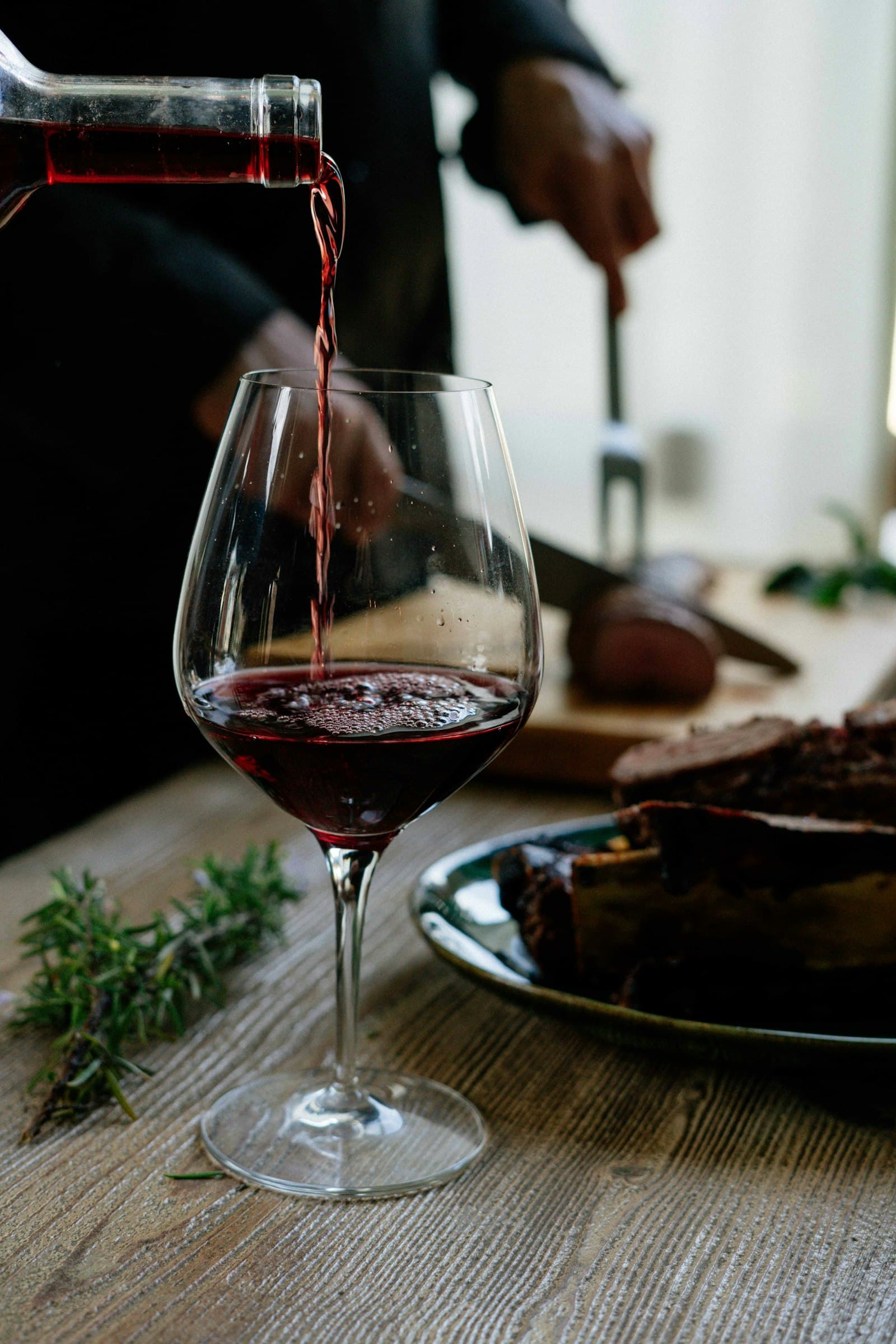 Red wine is poured into a glass beside a dinner table.